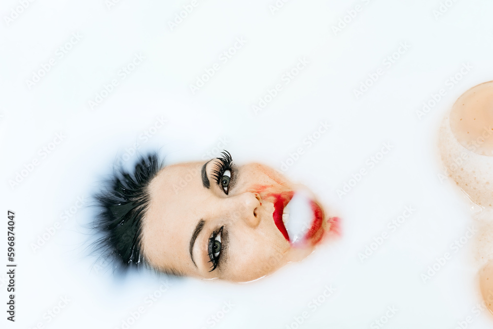 Woman's face in a milk. Portrait of beauty sexy woman with bright red lips in milk bath. Beautiful Fashion model girl taking milk bath, spa and skin care concept