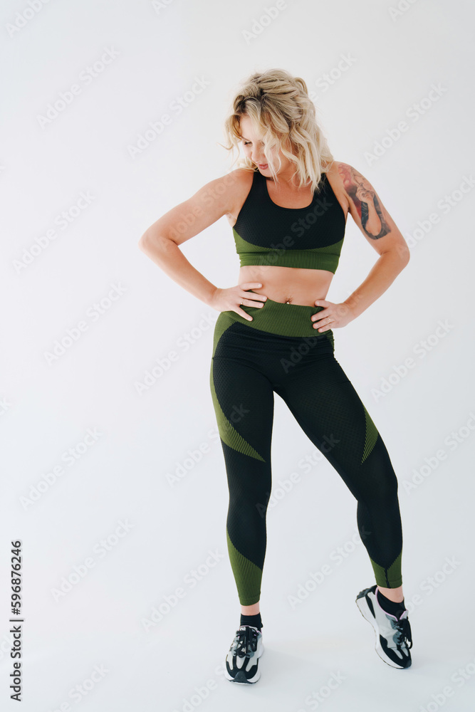 an attractive blonde in a black and green tracksuit poses on a white background. an attractive blonde in a black and green tracksuit poses on a white background.