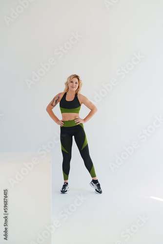 an attractive blonde in a black and green tracksuit poses on a white background.