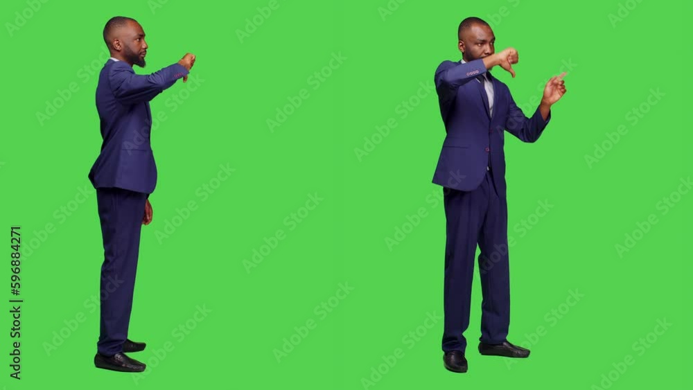 Negative office worker doing thumbs down in studio, wearing formal suit over greenscreen background. Young businessman showing dislike gesture and expressing disapproval on camera. Negative office worker doing thumbs down in studio, wearing formal suit over greenscreen background. Young businessman showing dislike gesture and expressing disapproval on camera.