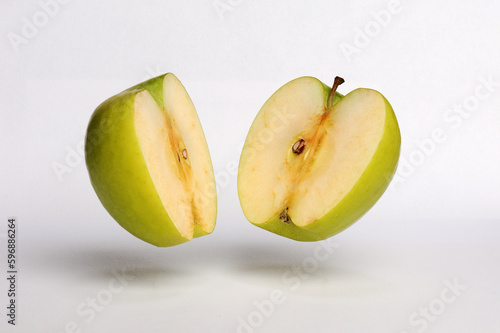 Green apple split in half on a white background, hovering