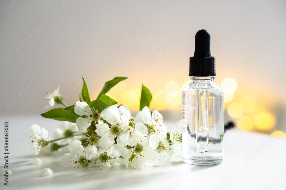 Clear glass cosmetic dropper bottle and white cherry flowers with bokeh lights, care product mockup