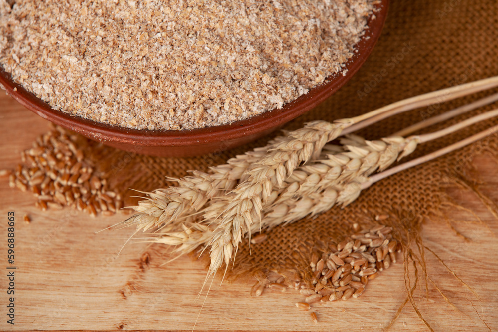 Wheat bran in a clay bowl and ears of wheat on a wooden background. Healthy food background. Food and baking ingredient.