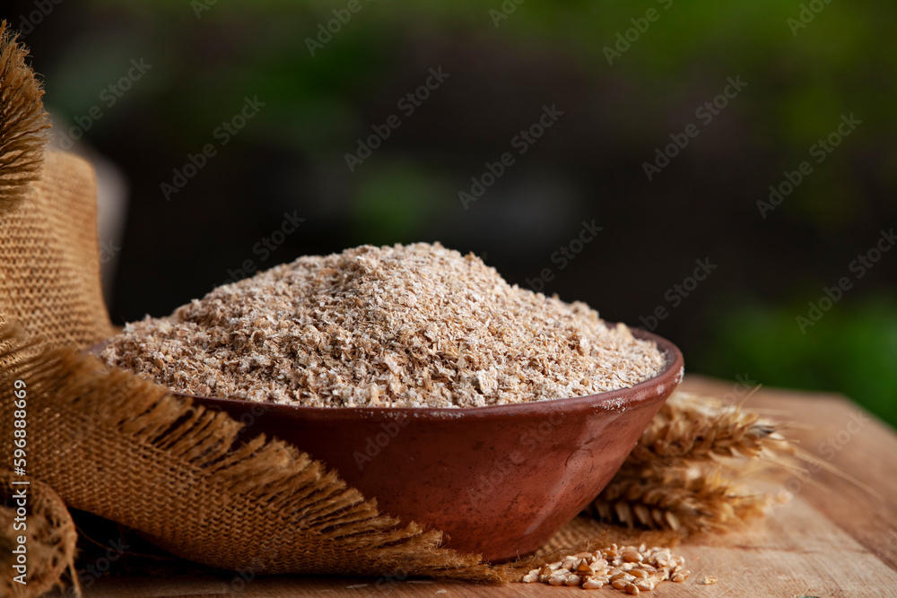 Wheat bran in a clay bowl and ears of wheat on a burlap background. Healthy food background. Food and baking ingredient.