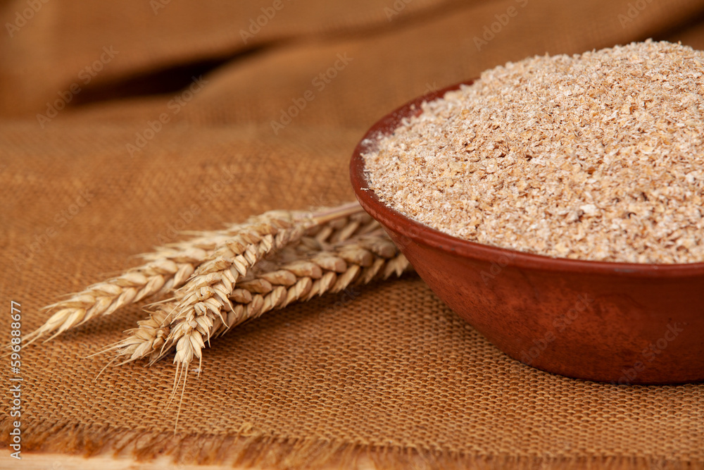 Wheat bran in a clay bowl and ears of wheat on a wooden background. Healthy food background. Food and baking ingredient.