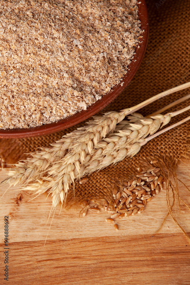 Wheat bran in a clay bowl and ears of wheat on a wooden background. Healthy food background. Food and baking ingredient.