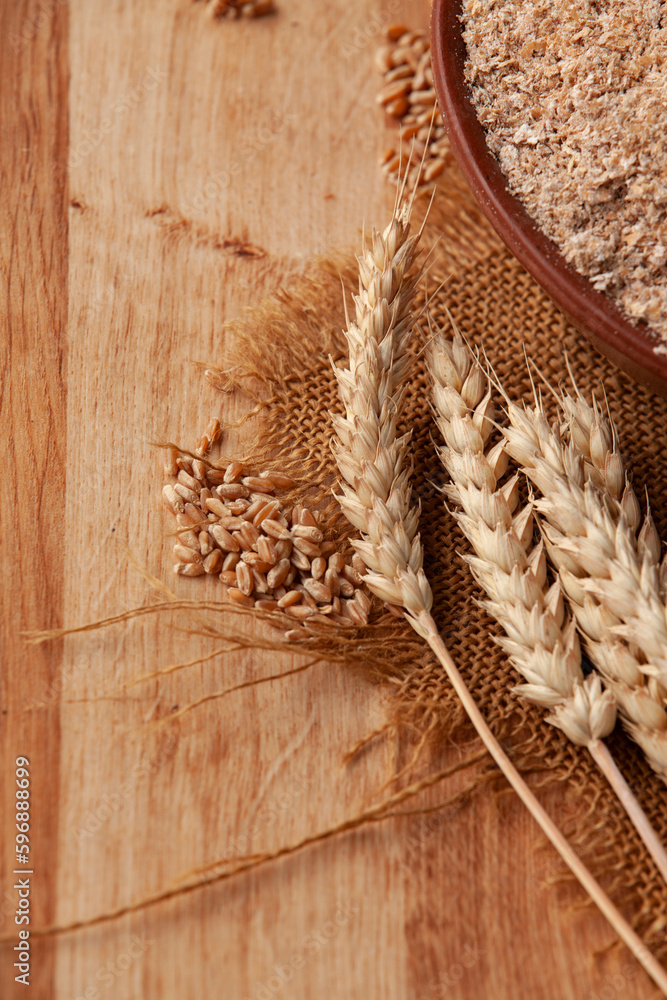 Wheat bran in a clay bowl and ears of wheat on a wooden background. Healthy food background. Food and baking ingredient.