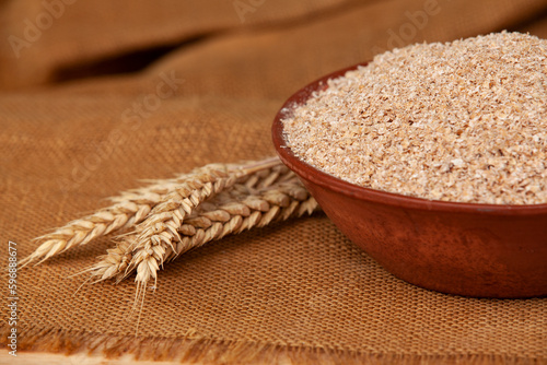 Obraz na płótnie Wheat bran in a clay bowl and ears of wheat on a wooden background. Healthy food background. Food and baking ingredient. w salonie