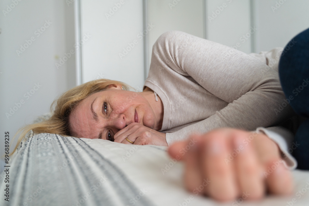 Mature woman curled lying on the bed at home top view. Depression, mental health, abuse problem Mature woman curled lying on the bed at home top view. Depression, mental health, abuse problem