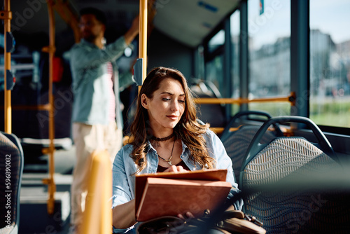 Young woman using digital tablet while riding in bus.