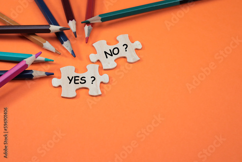 YES and NO are written on the missing puzzles on the orange background with colorful pencils at the side. Copy space for text and messages 