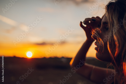 Cropped portrait of a young woman adjusting her hair in the summertime at sunset while posing in nature.