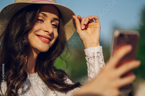 Portrait of a young trendy woman in summer style fashion clothes posing outdoors on a sunny summer day and taking selfies.