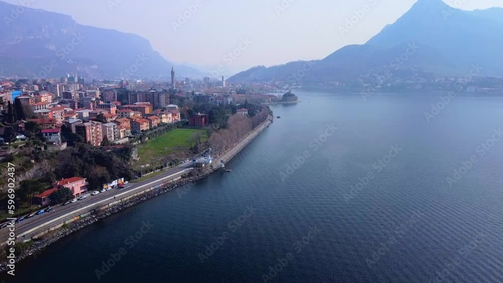 Aerial view of a beautiful european city near the shore of freshwater lake como in lombardy. Gothic church bell tower. Roofs of buildings. Mountains and rocks. Road by the water. Lecco Italy 11.2023 Aerial view of a beautiful european city near the shore of freshwater lake como in lombardy. Gothic church bell tower. Roofs of buildings. Mountains and rocks. Road by the water. Lecco Italy 11.2023