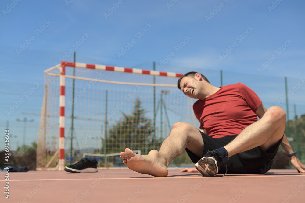 Stockfoto man wincing in pain sitting on the floor with injured ankle