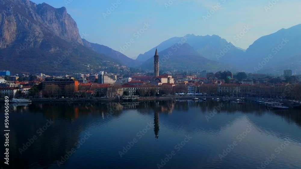 Aerial view of a beautiful european city near the shore of freshwater lake como in lombardy. Gothic church bell tower. Roofs of buildings. Mountains and rocks. Road by the water. Lecco Italy Aerial view of a beautiful european city near the shore of freshwater lake como in lombardy. Gothic church bell tower. Roofs of buildings. Mountains and rocks. Road by the water. Lecco Italy