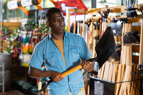 Portrait of african american man choosing shovel in gardening market