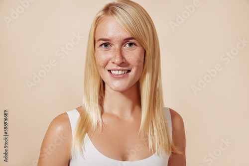 Portrait of a beautiful woman with freckles in studio. Young female with perfect skin against a beige backdrop.