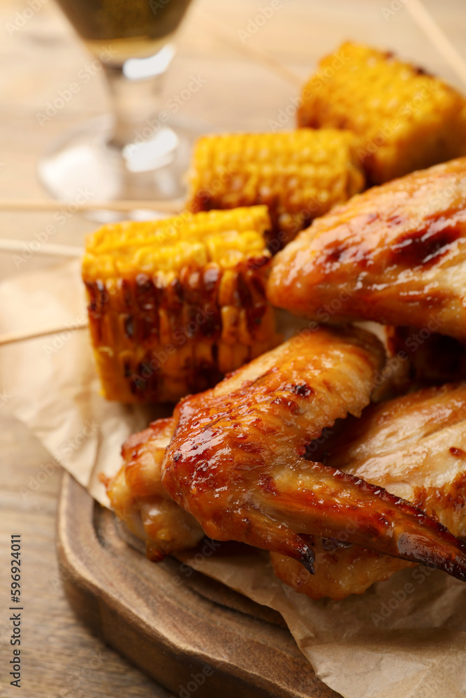 Delicious baked chicken wings and grilled corn served on wooden table, closeup Delicious baked chicken wings and grilled corn served on wooden table, closeup