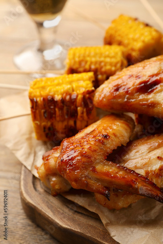 Delicious baked chicken wings and grilled corn served on wooden table, closeup