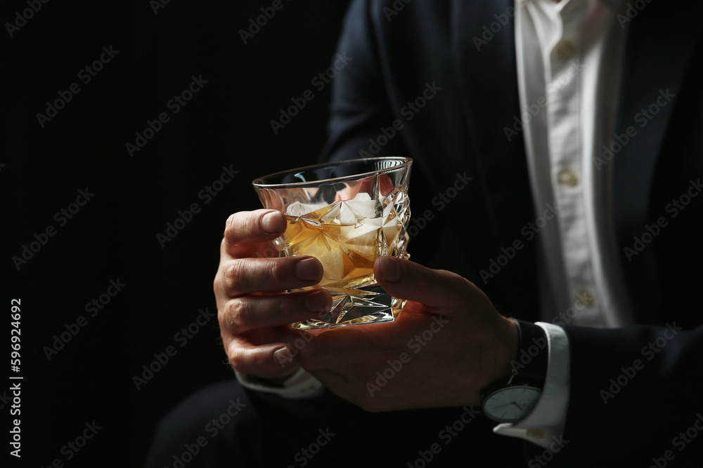 Man holding glass of whiskey with ice cubes on black background, closeup Man holding glass of whiskey with ice cubes on black background, closeup