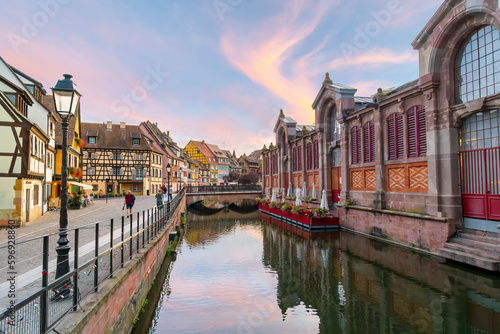 Picturesque half timber buildings across from the riverfront Marché Couvert covered market at sunset along the Lauch River in the Petite Venice area of Colmar, France.