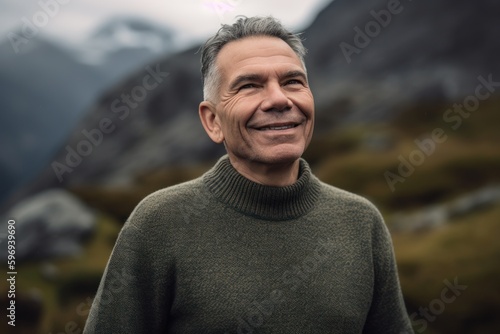 Portrait of a handsome mature man in a green sweater against the background of mountains