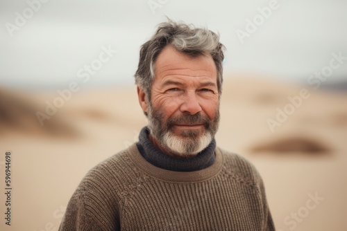 Portrait of a middle-aged man with grey hair and beard in a knitted sweater on the background of sand dunes