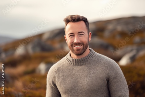 Portrait of a handsome young man with beard smiling at camera in the mountains