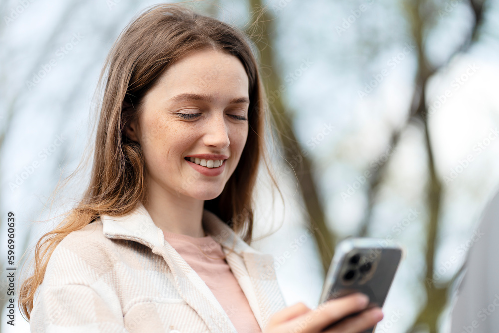 Beautiful smiling woman holding mobile phone, reading text message, communication online, watching video standing on the street. Happy confident female using mobile app shopping online outdoors Beautiful smiling woman holding mobile phone, reading text message, communication online, watching video standing on the street. Happy confident female using mobile app shopping online outdoors