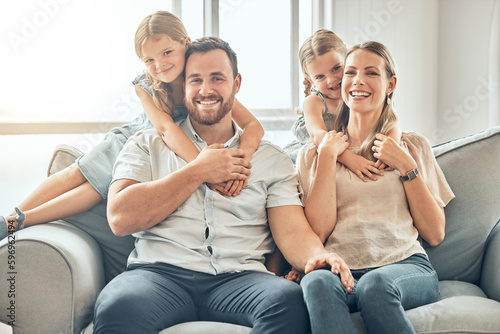 Happy family smiling while sitting close together on the sofa at home. Happy adorable girl sisters bonding with their mother and father on a weekend. Happy couple and daughters in the living room