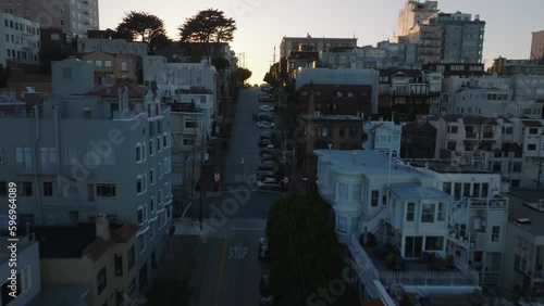 Forwards fly above steep street. Revealing residential urban borough against sunset.