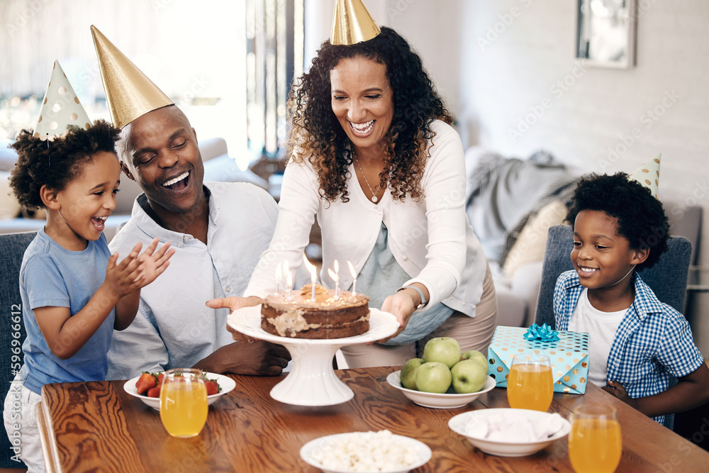 African american family celebrating birthday at home. Mom putting birthday cake with candles on table. . Two little boys and their parents wearing party hats and looking excited African american family celebrating birthday at home. Mom putting birthday cake with candles on table. . Two little boys and their parents wearing party hats and looking excited