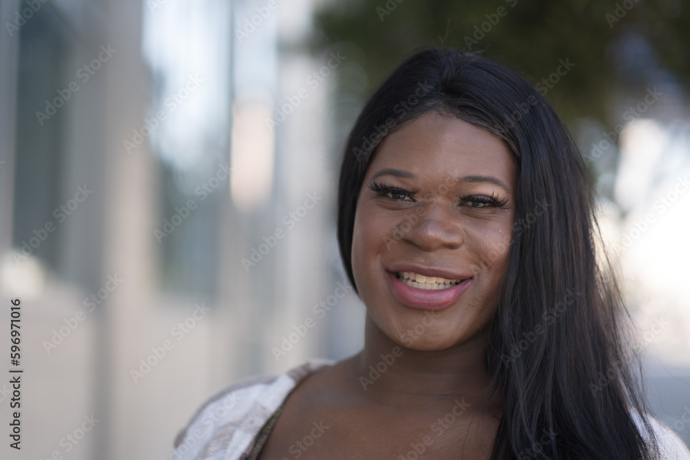 Smiling while posing outdoors on the sidewalk, a young African American transwoman showcases pride, happiness, and joy in her life. Smiling while posing outdoors on the sidewalk, a young African American transwoman showcases pride, happiness, and joy in her life.