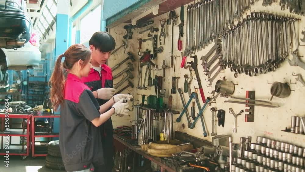Two professional Asian mechanic partners discuss hand tools and machinery for fixing work at car service garage, maintenance jobs, and check and repair occupation in automotive industry business. Two professional Asian mechanic partners discuss hand tools and machinery for fixing work at car service garage, maintenance jobs, and check and repair occupation in automotive industry business.