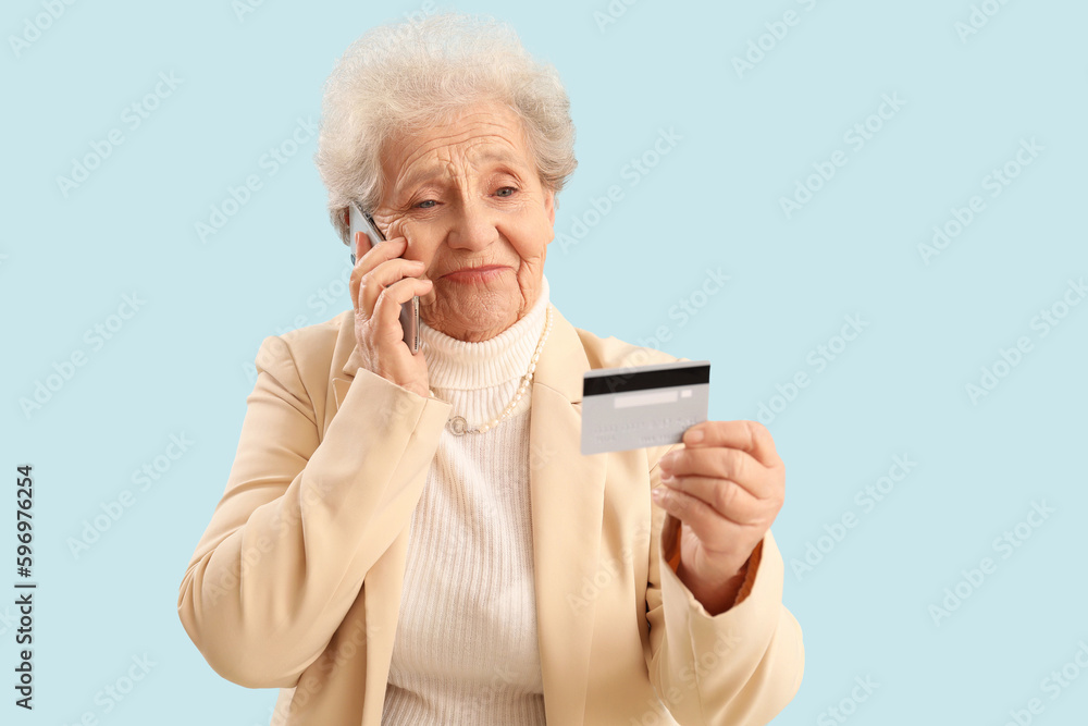 Senior woman with credit card talking by mobile phone on blue background Senior woman with credit card talking by mobile phone on blue background
