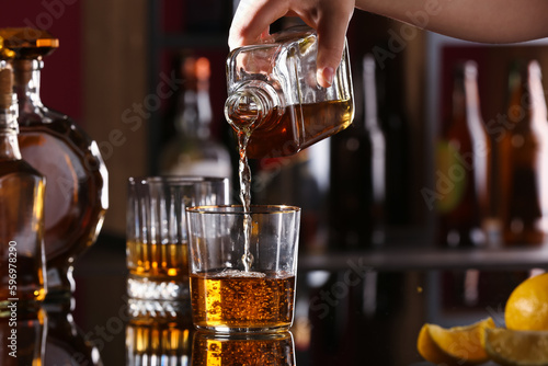 Woman pouring tasty rum from bottle into glass at table in bar