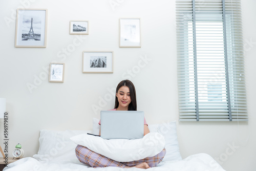 Asian attractive woman using laptop chat on bed at home in the morning. 