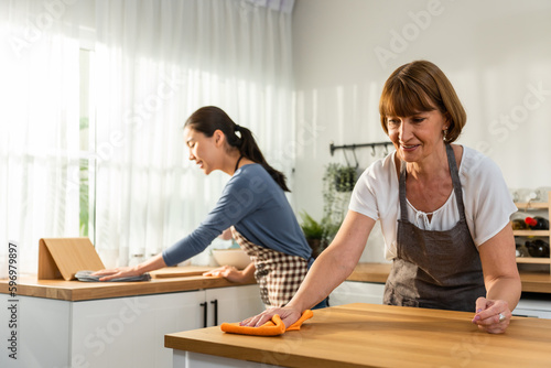 Caucasian senior elderly woman cleaning kitchen in house with daughter. 