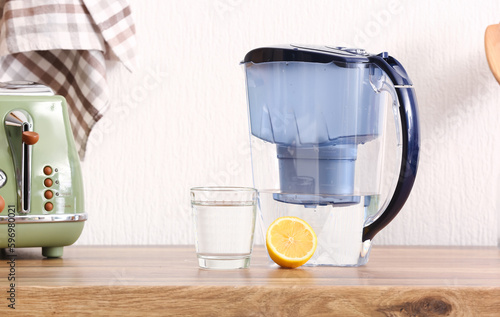 Modern filter jug, glass of water and lemon on kitchen counter