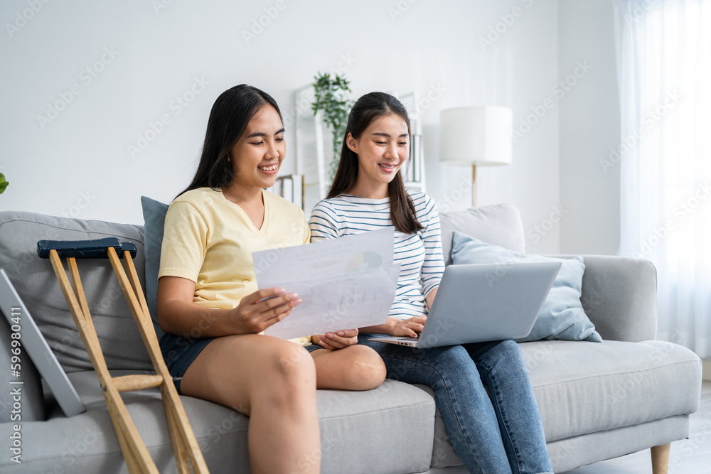 Asian woman amputee using laptop computer with friend in living room. Asian woman amputee using laptop computer with friend in living room.