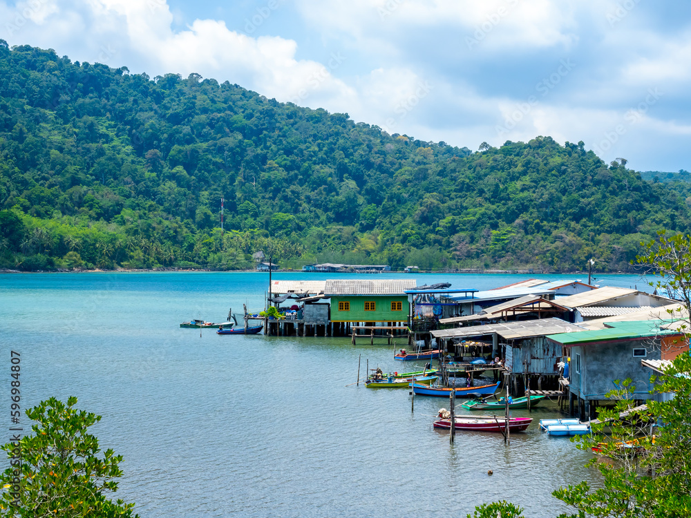 Ao Yai village, Koh kood, trat, Thailand. Scene of fisherman local village with many house in the tropical blue sea and green mountain with beautiful view with open sky on summer sunshine day. Ao Yai village, Koh kood, trat, Thailand. Scene of fisherman local village with many house in the tropical blue sea and green mountain with beautiful view with open sky on summer sunshine day.