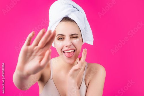 Funny model applying cosmetic cream treatment on face. Facial treatment. Beauty portrait of young topless woman with bare shoulders applying face cream.