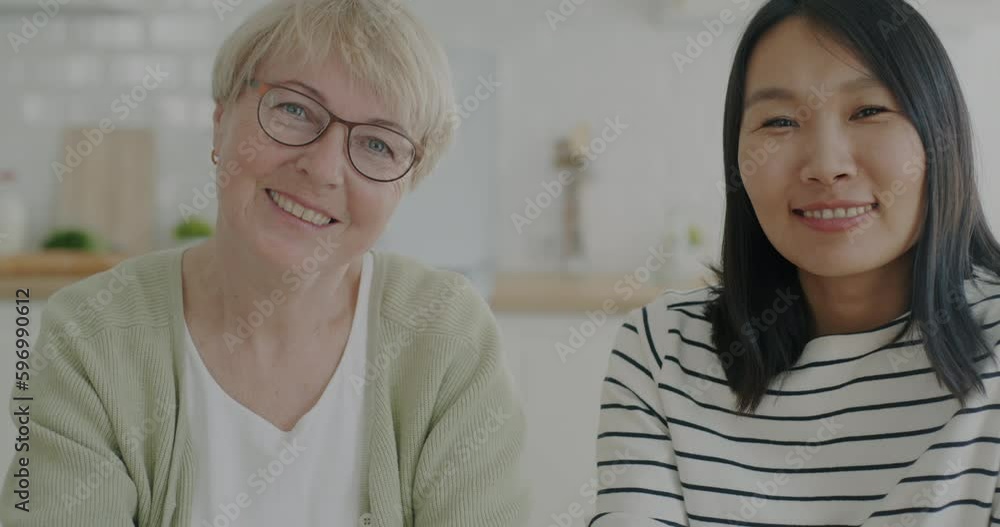 Slow motion portrait of cheerful women Asian and Caucasian smiling looking at camera with happiness in kitchen at home. People and family concept. Slow motion portrait of cheerful women Asian and Caucasian smiling looking at camera with happiness in kitchen at home. People and family concept.