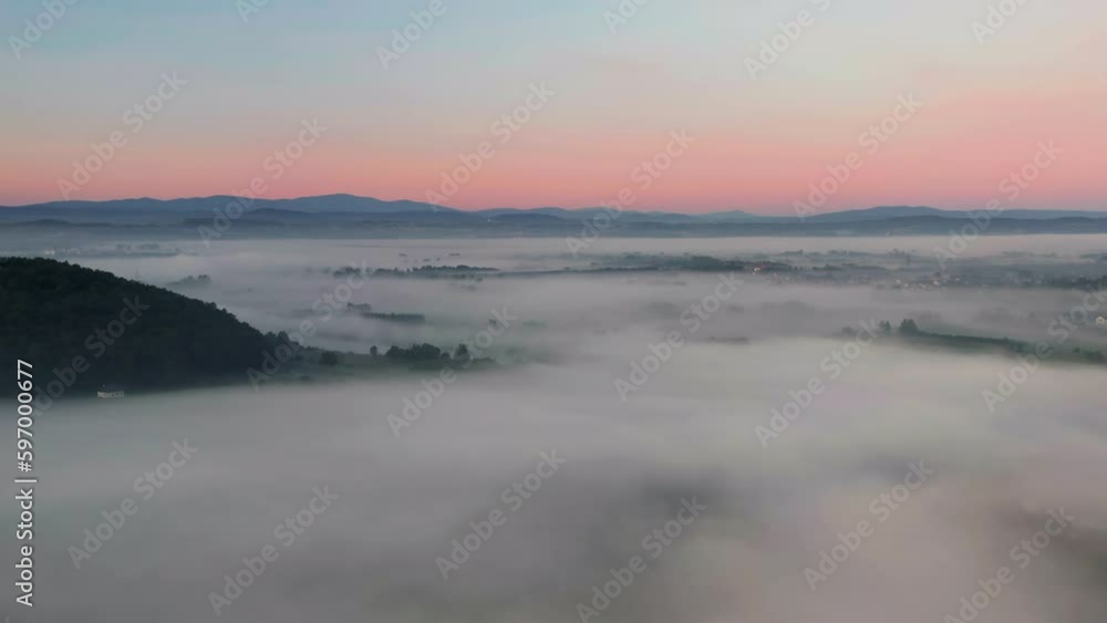 Slow, aerial view of town in valley covered by mist with mountain view at sunrise. Tyniec, near Krakow in Poland Slow, aerial view of town in valley covered by mist with mountain view at sunrise. Tyniec, near Krakow in Poland