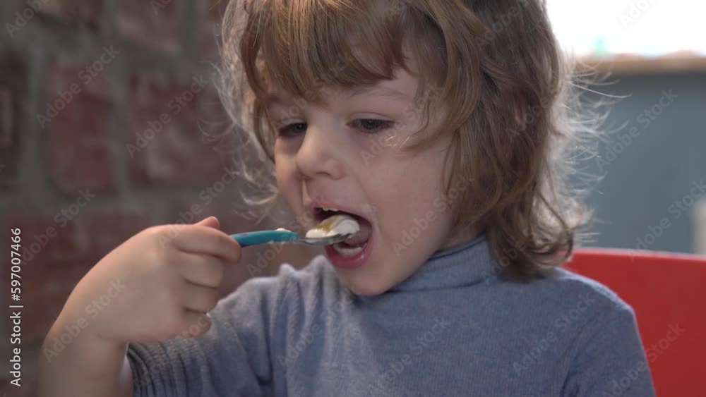 a little boy is interestedly looking at the tablet and eats yogurt a little boy is interestedly looking at the tablet and eats yogurt