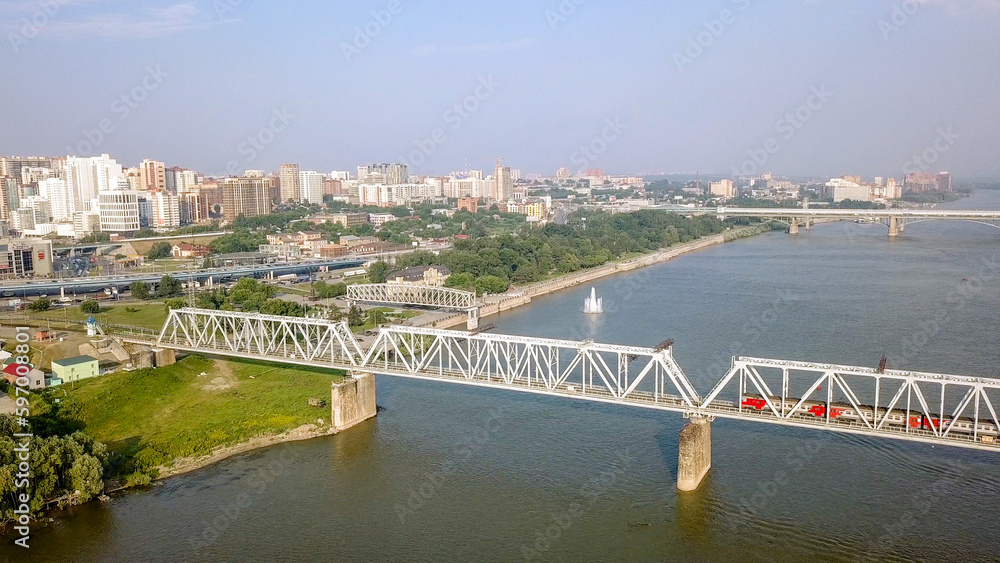 The electric train crosses the Ob river. First Railway Bridge in Novosibirsk. Panorama of the city of Novosibirsk. Russia, From Dron
