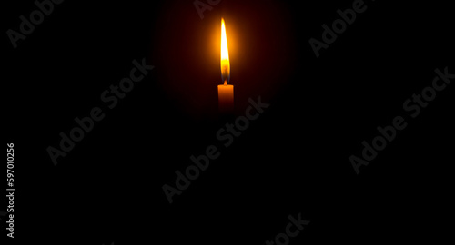 A single burning candle flame or light glowing on an orange candle on black or dark background on table in church for Christmas, funeral or memorial service with copy space