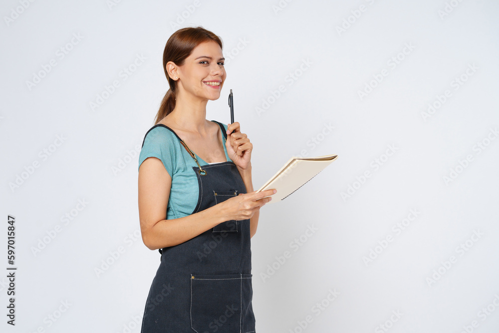 Young woman wearing kitchen apron holding notepad recipe cooking book and pen isolated on white background Young woman wearing kitchen apron holding notepad recipe cooking book and pen isolated on white background