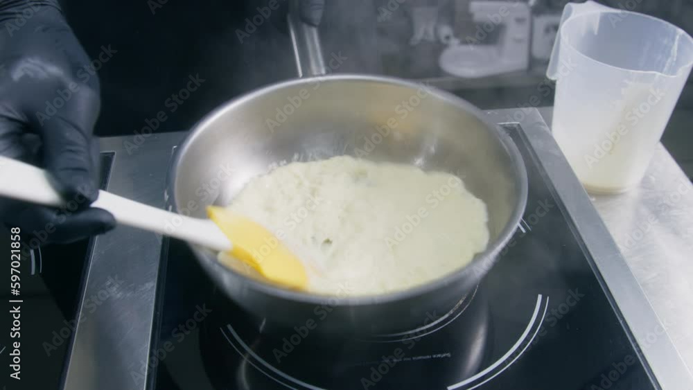 Male cook fries and stirs scrambled eggs into frying pan on induction stove. Chef cooks delicious breakfast dish. Cooking process on restaurant or cafe kitchen. Professional cuisine. Public catering. Male cook fries and stirs scrambled eggs into frying pan on induction stove. Chef cooks delicious breakfast dish. Cooking process on restaurant or cafe kitchen. Professional cuisine. Public catering.